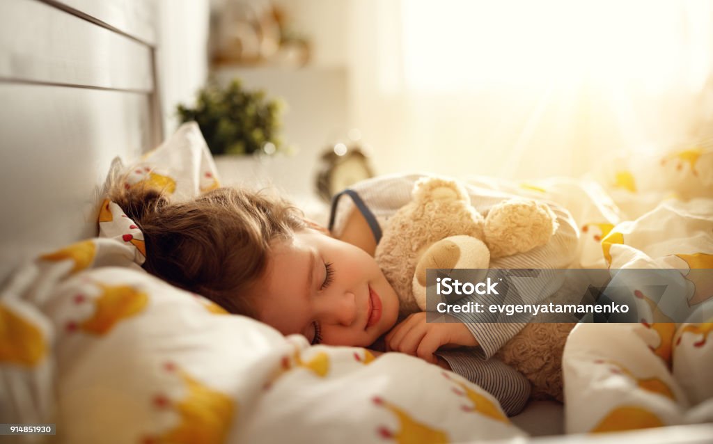 child  girl sleeps in her bed with toy teddy bear  in morning child  girl sleeps in her bed with a toy teddy bear  in morning Child Stock Photo