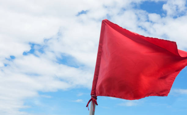 istock Red warning flag waving on the blue sky with clouds 914852484