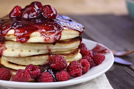 Delicious homemade golden pancakes with fresh raspberries and raspberry syrup. Extreme shallow depth of field.