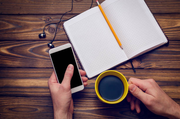 istock A hand holds a smartphone and a cup of coffee over a wooden table with a notebook 914862798