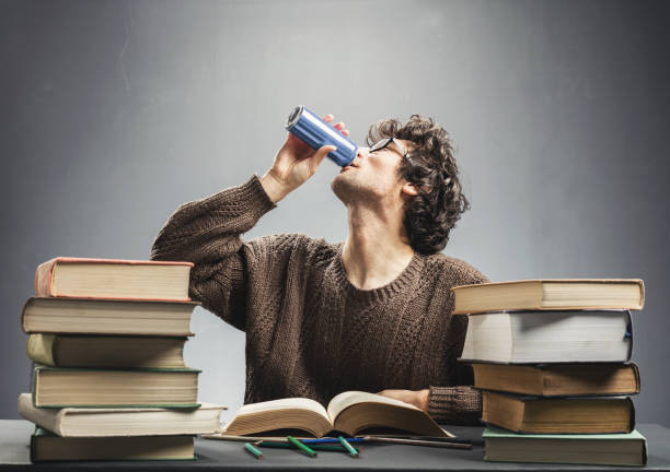 Young man studying and drinking energy drink. Young man drinking energy drink while studying. College student concept. Energizing before learning. energy drink stock pictures, royalty-free photos & images