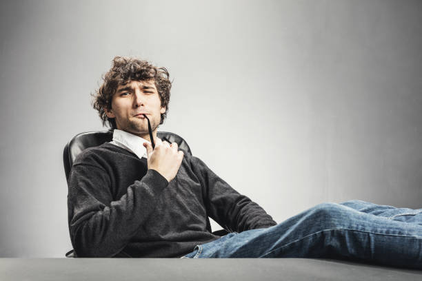 Relaxed man sitting with his legs laying on the table, chewing his glasses.