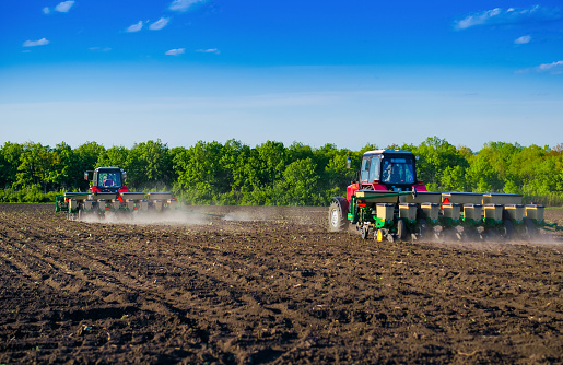 Two modern tractors plow fertile soil for sowing seeds.