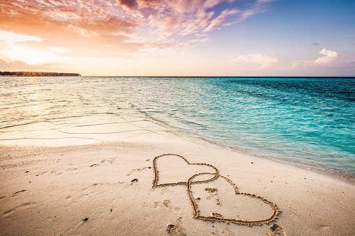 Two hearts drawn on a sandy beach by the sea. Sunset view. Love symbol.