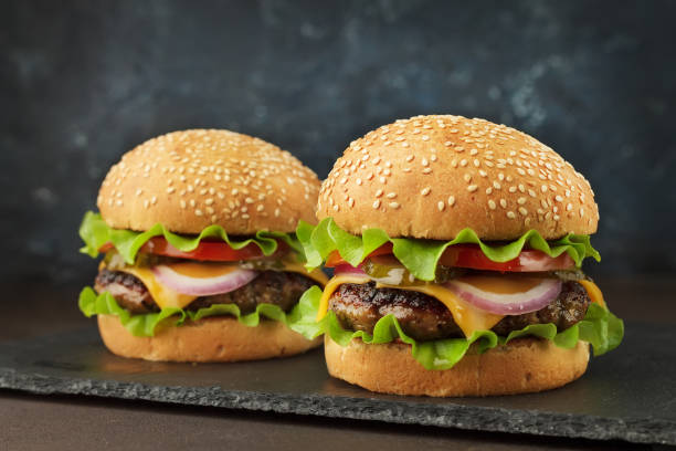 istock Homemad fast food: two burgers with beef, cheddar, lettuce, onion ang tomato on the slate board. 914877020