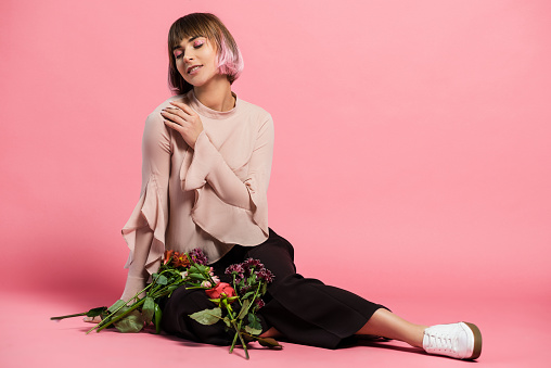 Young attractive woman in fashionable clothes sitting on floor with bunch of bright flowers