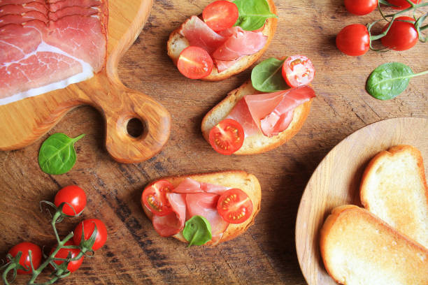 bruschetta with prosciutto ham, cherry tomatoes and green spinach . top view - bruschetta cutting board italy olive oil imagens e fotografias de stock