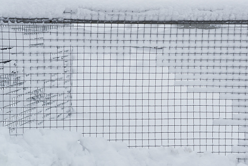 The fence net is covered with snow.