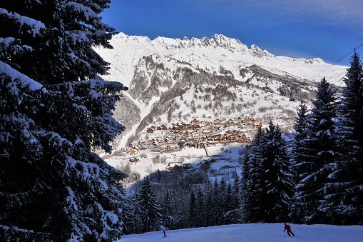 Alpe d’Huez, France - February 2, 2018: View from a tree-lined section of the La Fare piste looking across the valley to the village of Vaujany on the opposite mountainside. This was taken the morning after a fresh snowfall. The Vaujany - Alpette cable car is visible on the right tree-top line.