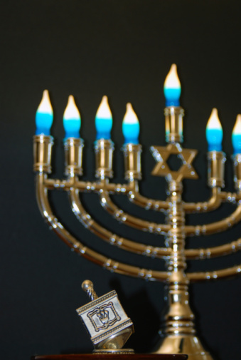 Lit shabbat candles on silver candlesticks on blue print cloth and wooden table