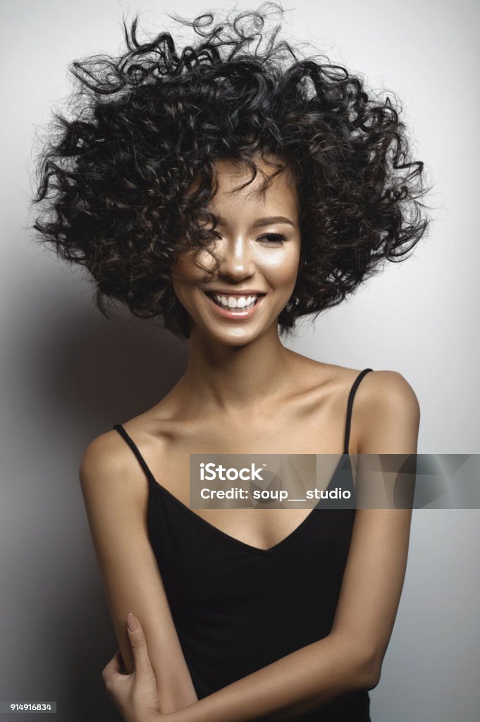 Smiling woman in black dress with afro curls hairstyle Fashion studio portrait of beautiful smiling woman in black dress with afro curls hairstyle. Fashion and beauty Women Stock Photo