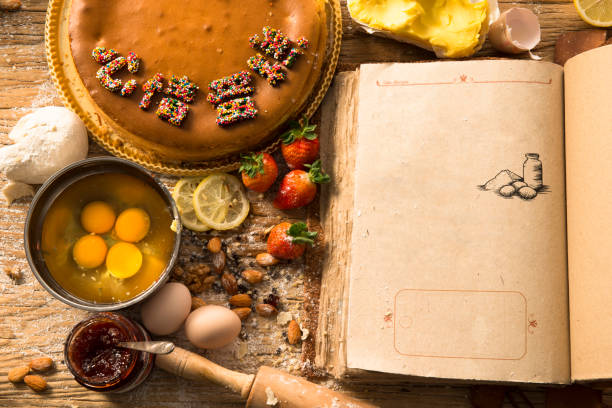 istock Rural vintage wooden kitchen table with old blank book and baking cake ingredients (strawberry, eggs, flour, milk, butter, sugar). Background layout with free recipe text space. 914918090