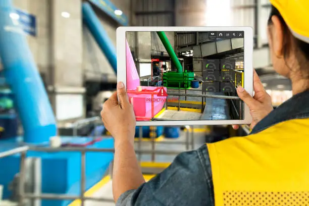 Industrial 4.0 , Augmented reality concept. Hand holding tablet with AR service , maintenance application and calling technician for check destroy part of smart machine in smart factory background.