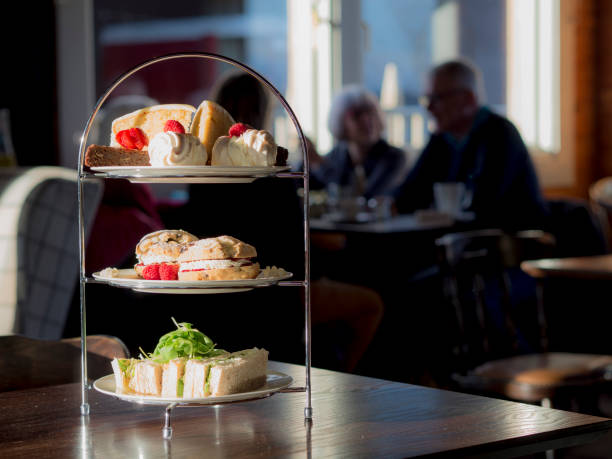 Afternoon Tea with people in the background. Afternoon Tea featuring sandwiches, scones, jam, strawberries, raspberries, chocolate brownie, merengue and cake on a cake stand using natural light. afternoon tea stock pictures, royalty-free photos & images