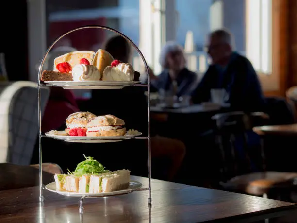 Afternoon Tea featuring sandwiches, scones, jam, strawberries, raspberries, chocolate brownie, merengue and cake on a cake stand using natural light.