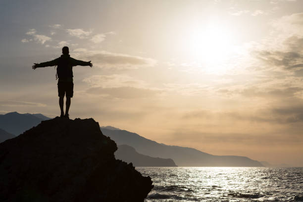 伸ばした腕を持�つ男を祝う山日の出 - mountain looking at view beach cliff ストックフォトと画像