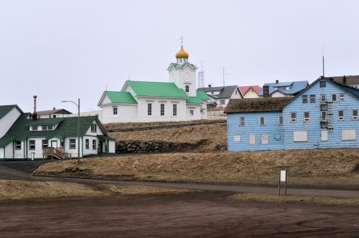 The old town on St Paul Island in Alaska with a Russian Orthodox church above(where else) the village. Some buildings are freshly painted, other are well weathered. A wooden fire escape (go figure) is present on the foremost building.