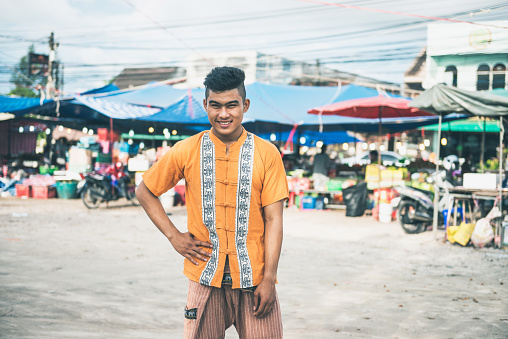 Portrait of young farmer or green market salesman, who is selling fresh fruits and vegetables on the market in small town in South East Asia. Cheerful young man is making money with selling his home grown farm products