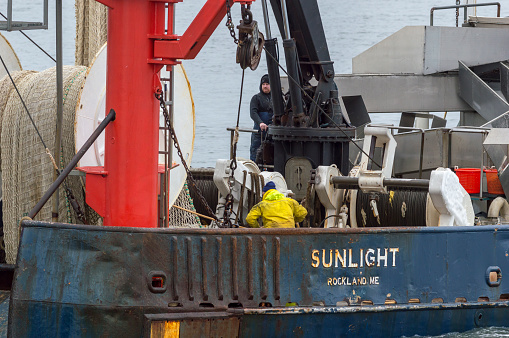 New Bedford, Massachusetts, USA - February 4, 2018: Crewmen secure gear as commercial fishing vessel Sunlight, hailing port Rockland, Maine, crosses New Bedford harbor