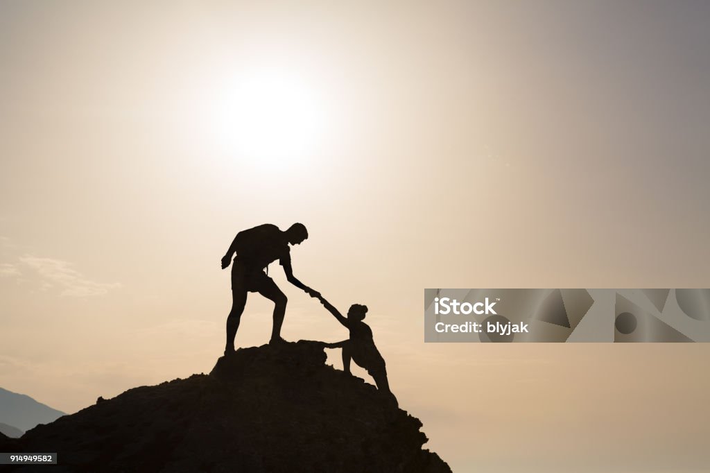 Teamwork couple helping hand trust in inspiring mountains Teamwork couple helping hand trust silhouette in inspiring mountains. Team of climbers assistance man and woman hiker, help each other on top of mountain, beautiful sunrise landscape in Crete Greece Trust Stock Photo
