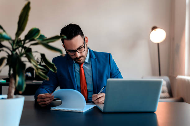 istock Pensive young handsome man writing in his notebook while sitting at his working place. 914952648