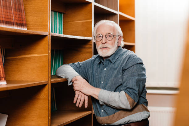 istock grey hair librarian leaning on shelves and looking at camera 914985722