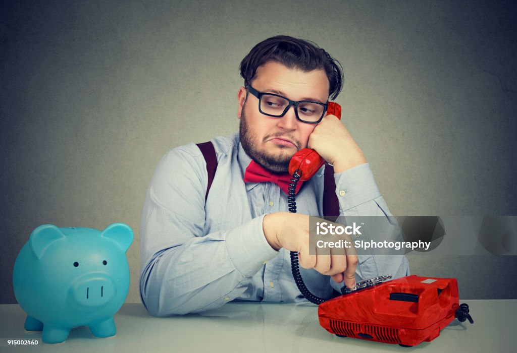 Bank worker having phone call Sly young business man sitting at desk with moneybox and talking on phone callling a client. Collection Stock Photo