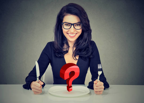 istock Happy woman in glasses with fork and knife sitting at table with empty plate 915002560