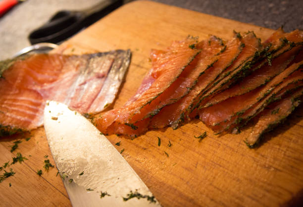 A cured slice of salmon gravlax with a herb cure sits on a wooden chopping board with a knife that has been used to cut it.