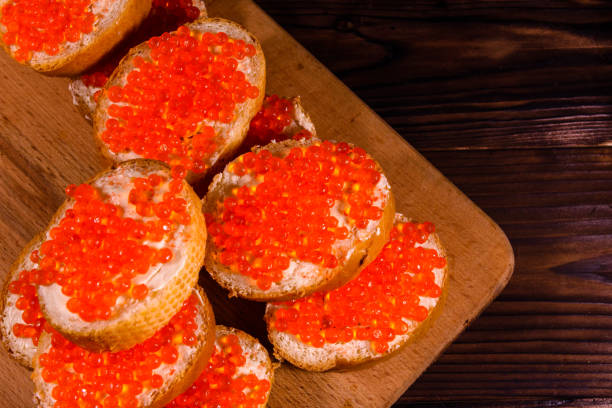 sándwiches con caviar rojo en una tabla de cortar - plank bread caviar close up fotografías e imágenes de stock