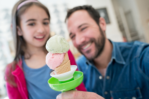 Single dad and daughter enjoying a delicious ice cream cone at the ice cream parlor smiling very happy - Focus on foreground