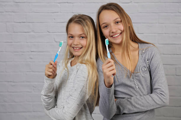 ritratto di due belle ragazze bambini con sorriso perfetto tenendo spazzolini da denti. cura dentale per bambini, concetto di igiene orale - lifestyles toothy smile care beauty foto e immagini stock