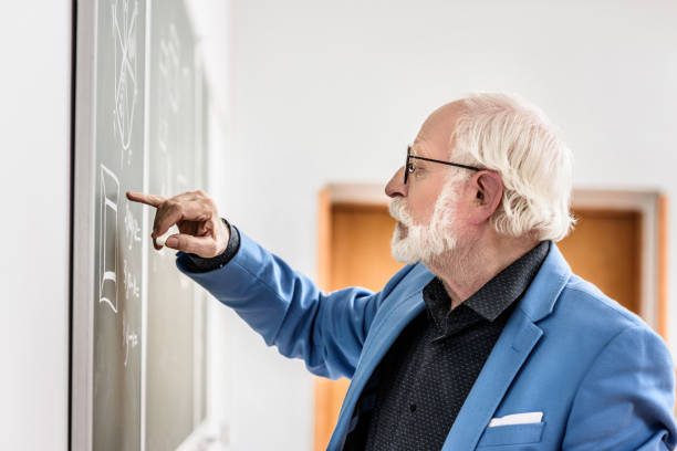 istock side view of grey hair professor correcting something at blackboard 915017750
