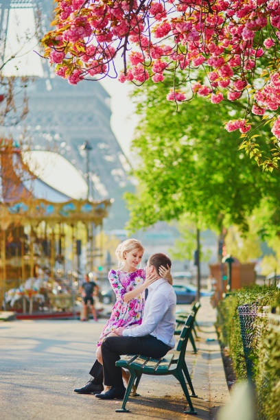 Couple near the Eiffel tower on spring day in Paris Beautiful romantic couple under blooming cherry tree on a spring day with Eiffel tower in background in Paris, France holding child flower april stock pictures, royalty-free photos & images