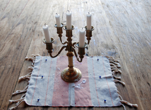 A Menorah burning all eight candles and Shamash to celebrate Hanukkah sitting on a stained wooden fireplace mantel along with a Dreidel and blue pouch with gold coins spilling out.