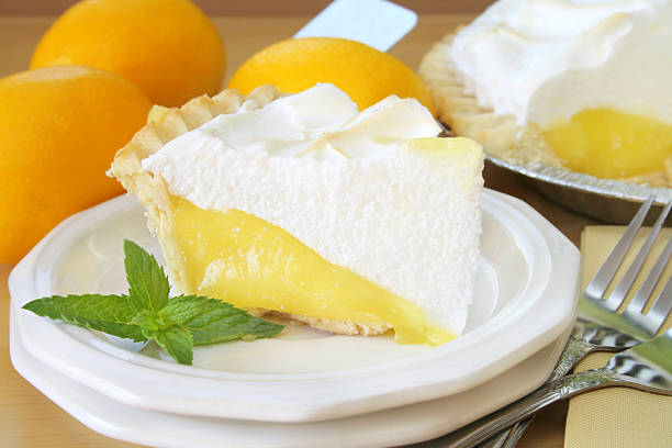 Slice of lemon meringue pie on plate with forks Close up of a slice of lemon meringue pie garnished with fresh mint leaves.  In the background there is lemons and the pie that the slice came from. meringue stock pictures, royalty-free photos & images