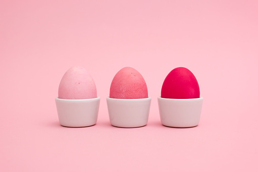 Row of egg cups with three eggs colored in different shades of pink