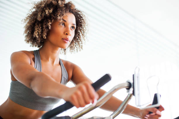 woman doing cardio exercises on a stationary bike at the gym - bicycle women cycling gym imagens e fotografias de stock