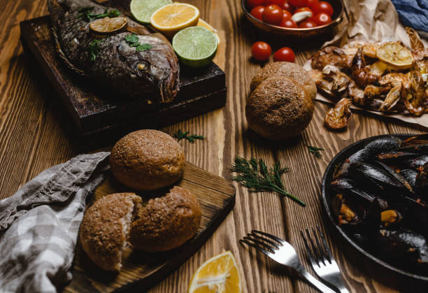 istock Assorted seafood and baked fish with bread and tomatoes on wooden table 915032088