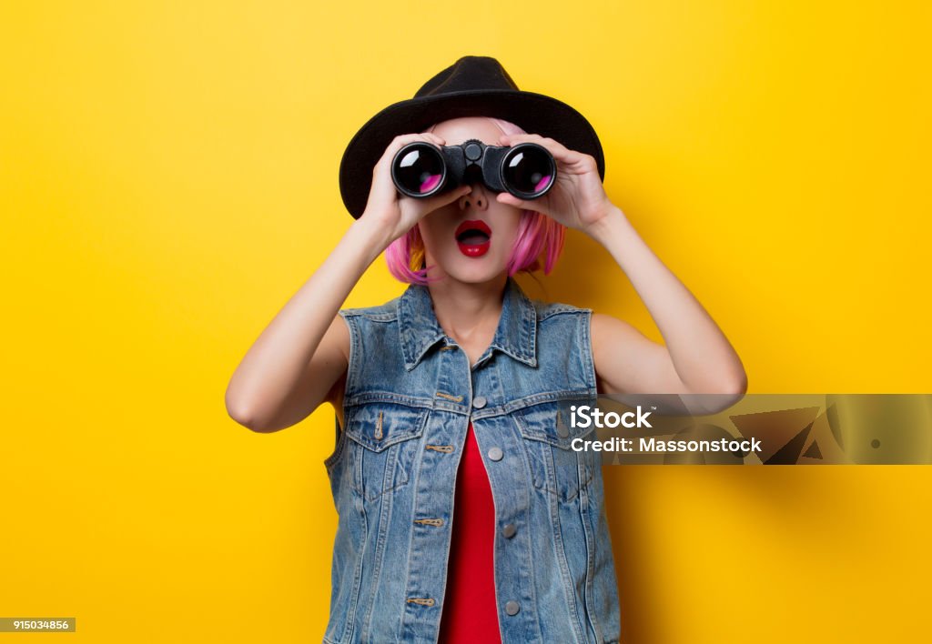 hipster girl with pink hair style with binoculars Portrait of young style hipster girl with pink hair style with binoculars on yellow background Binoculars Stock Photo