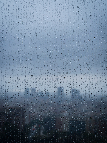 After heavy rainfall, the diffuse distant skyline of Barcelona is emerging in the twilight behind raindrops on a window.