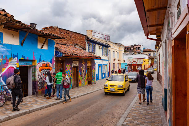 bogotá, colombia - coche coches y gente a pie a través de una de las coloridas calles del histórico distrito la candelaria en la ciudad capital - graffiti paintings men walking fotografías e imágenes de stock