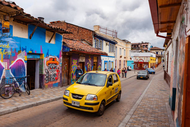 bogotá, colombia - un taxi pequeño conduce encima de una de las coloridas calles del histórico distrito la candelaria en la ciudad capital - graffiti paintings men walking fotografías e imágenes de stock