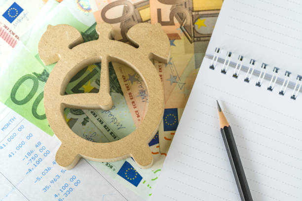 время для инвестирования, расчета налогов и долгов, карандаш на белой блокнотной бумаге с деревянным будильником на евро и зарплатный лист� - currency euro symbol european union currency calculator стоковые фото и изображения
