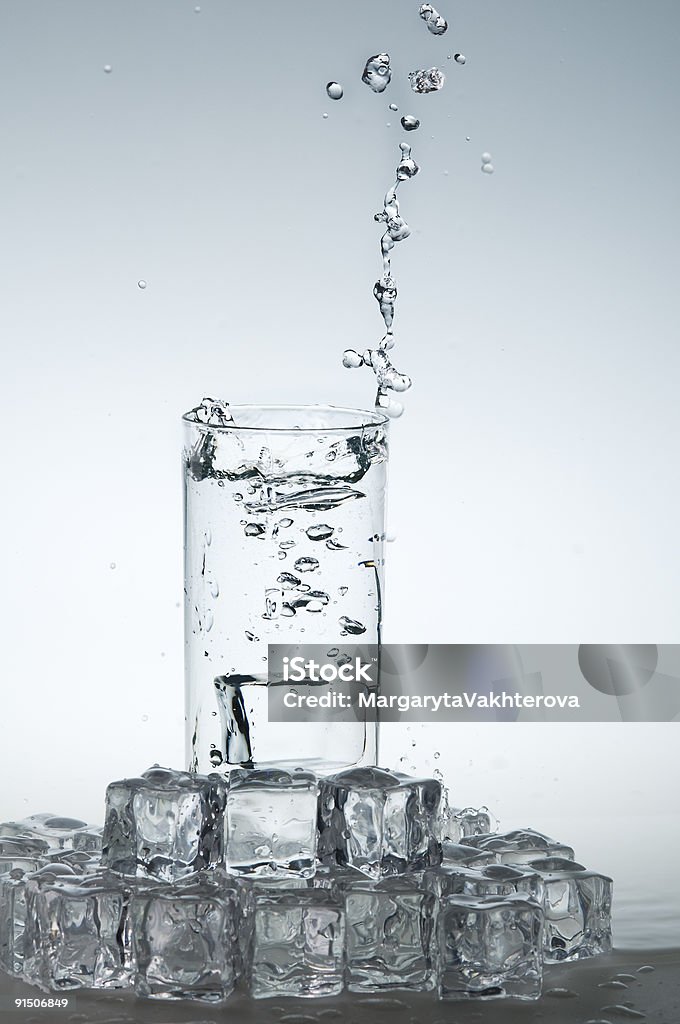 Acqua minerale schizzare fuori dal bicchiere con un cubetto di ghiaccio. - Foto stock royalty-free di Acqua potabile