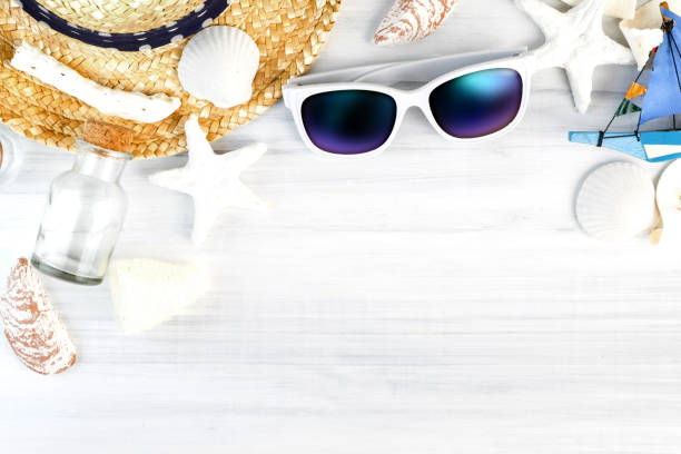 istock Summer Beach accessories (White sunglasses,starfish,straw hat,glass bottle,shell) on white plaster wood table top view,Summer vacation concept,Leave space for adding text.. 915071656