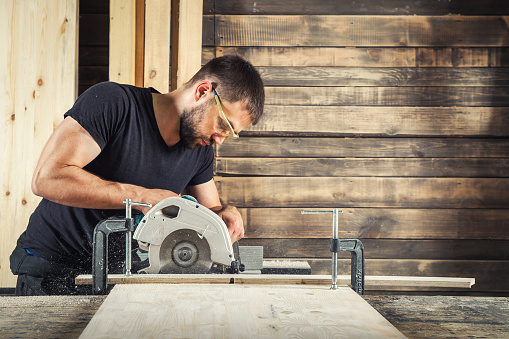 A man builder saws a board with a circular saw in the workshop