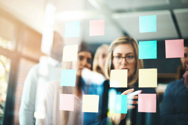 Marketing ideas that match the company brand Shot of a group of businesspeople arranging sticky notes on a glass wall in a modern office mind map photos stock pictures, royalty-free photos & images