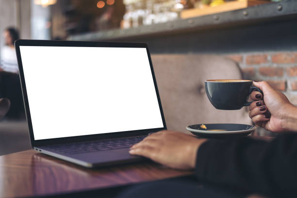 istock Mockup image of a businesswoman using laptop with blank white desktop screen while drinking hot coffee on wooden table in cafe 915090346