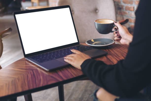 istock Mockup image of a businesswoman using laptop with blank white desktop screen while drinking hot coffee on wooden table in cafe 915090420